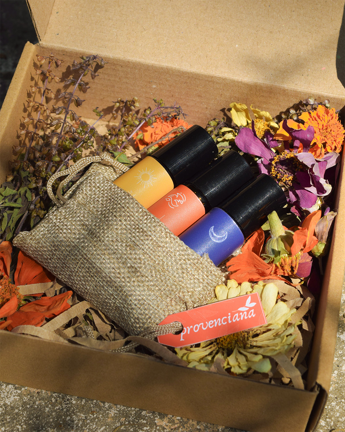 Close-up of the Halimuyak Ritual Trilogy oil rollers tucked into a small burlap pouch, presented in a gift box with dried Filipino botanicals and petals.